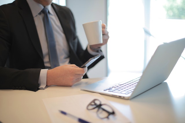 person holding a coffee cup and phone while looking at their open laptop